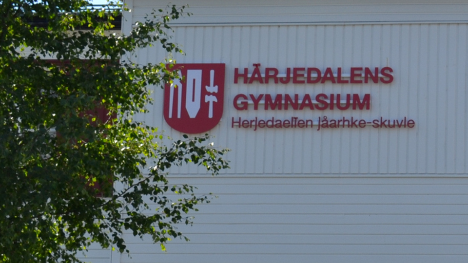 Logotyp Härjedalens gymnasium på vit träbyggnad.
