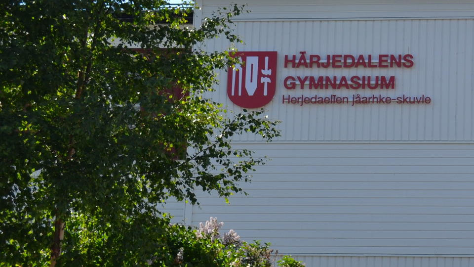 Texten Härjedalens gymnasium med kommunens logotyp i rött på vit träfasad.