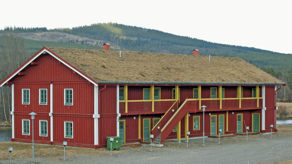 Rött flerfamiljshus vid Ljusnans strand med torvtak.