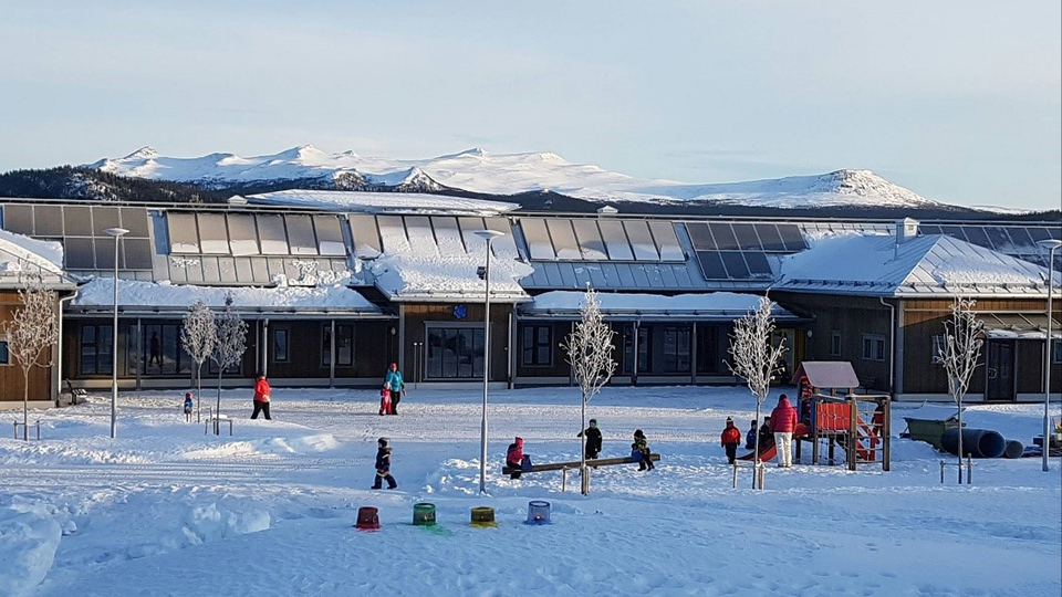 Barn leker på snöig skolgård. Fjäll i bakgrunden.
