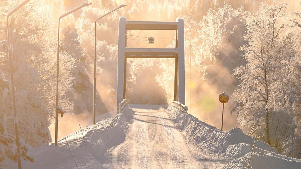 Snöig väg och en bågbro i kallt vinterklimat.