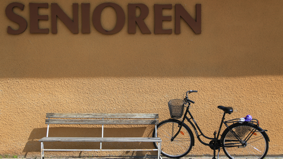 Gul rappad fasad med en träbänk, en parkerad cykel och texten Senioren på väggen.