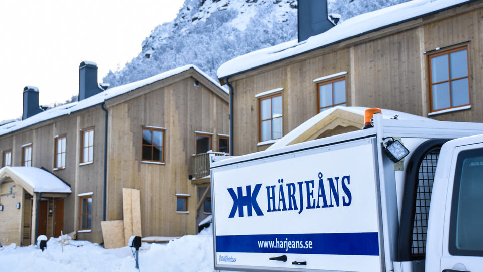 Bil med logotyp Härjeåns parerad framför nybyggda hus i vintermiljö.