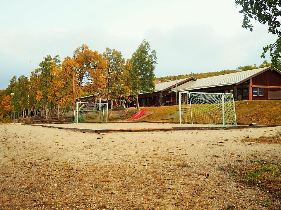 Förskola omgiven av träd i höstfärger, rutschkana och mindre fotbollsplan i förgrunden.